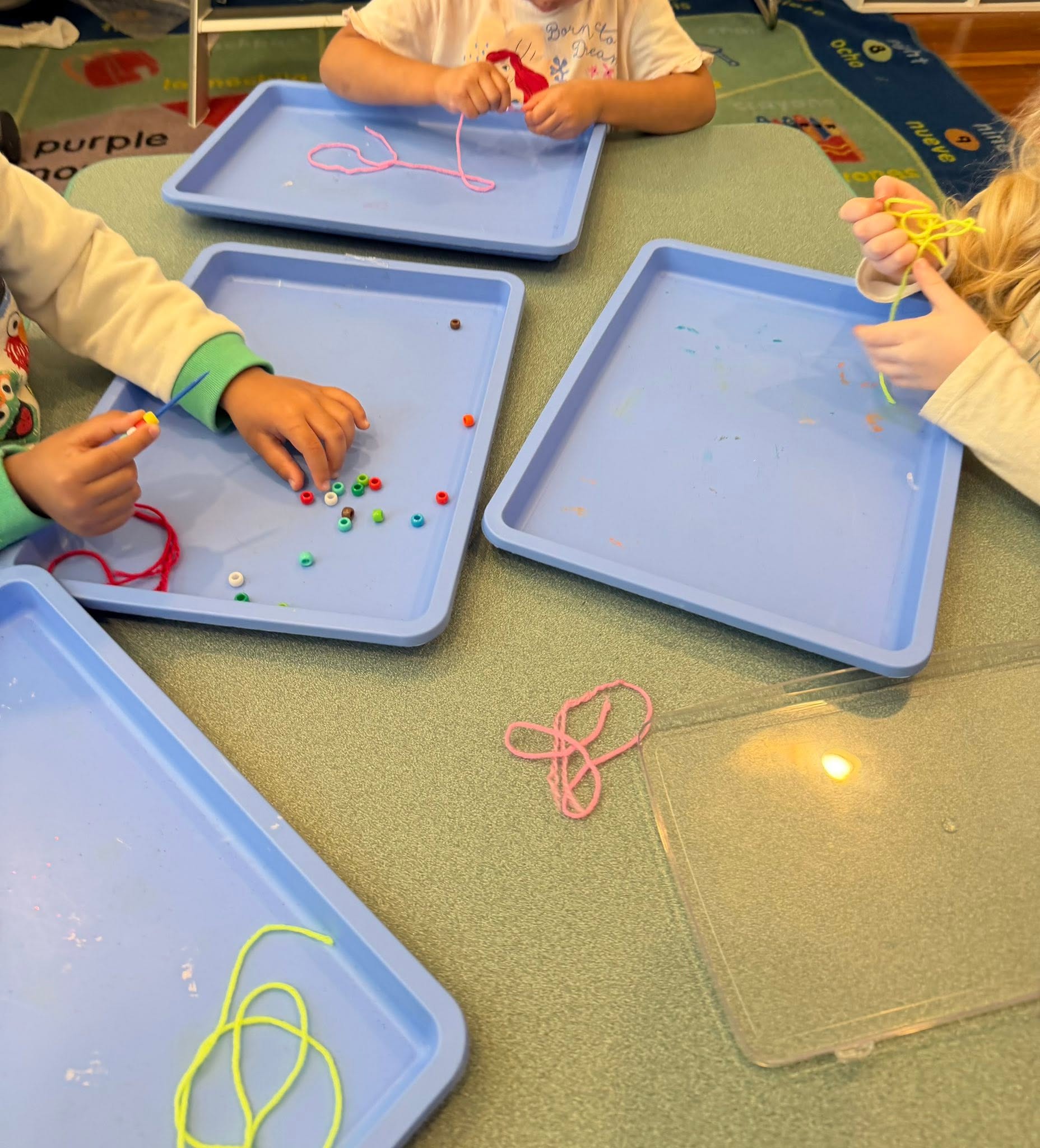 Small hands threading colored beads onto string at individual blue trays