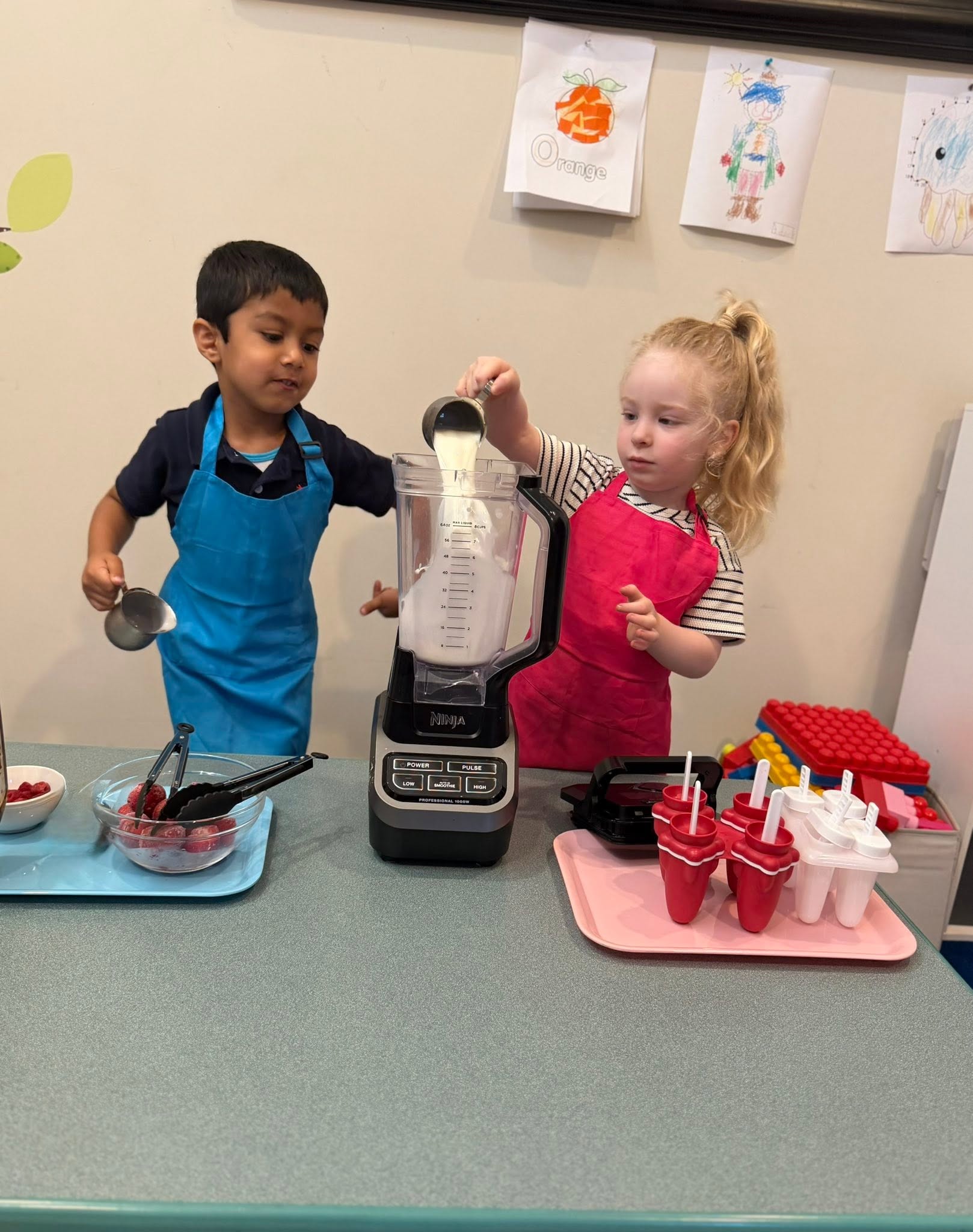 Two children in aprons using a blender to make fruit popsicles