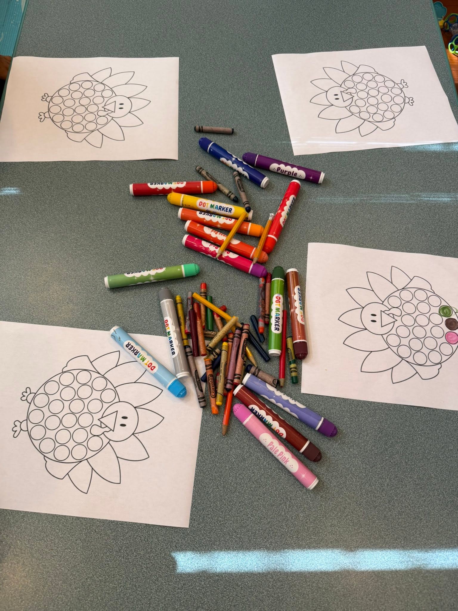 Turkey coloring sheets surrounded by dot markers and crayons on a table
