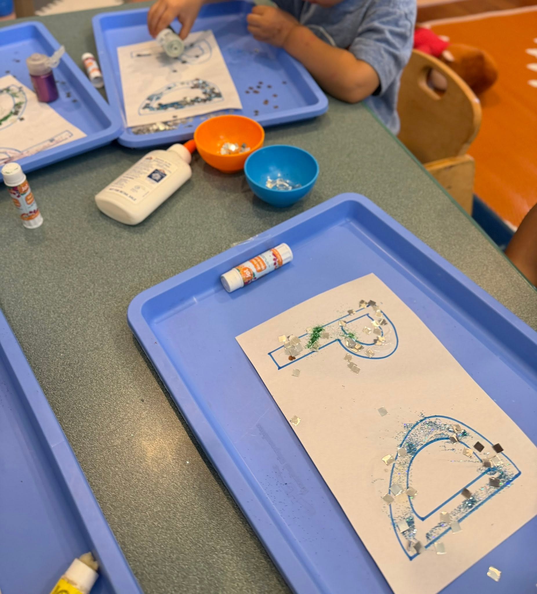 A letter worksheet decorated with glitter and sequins on a work tray