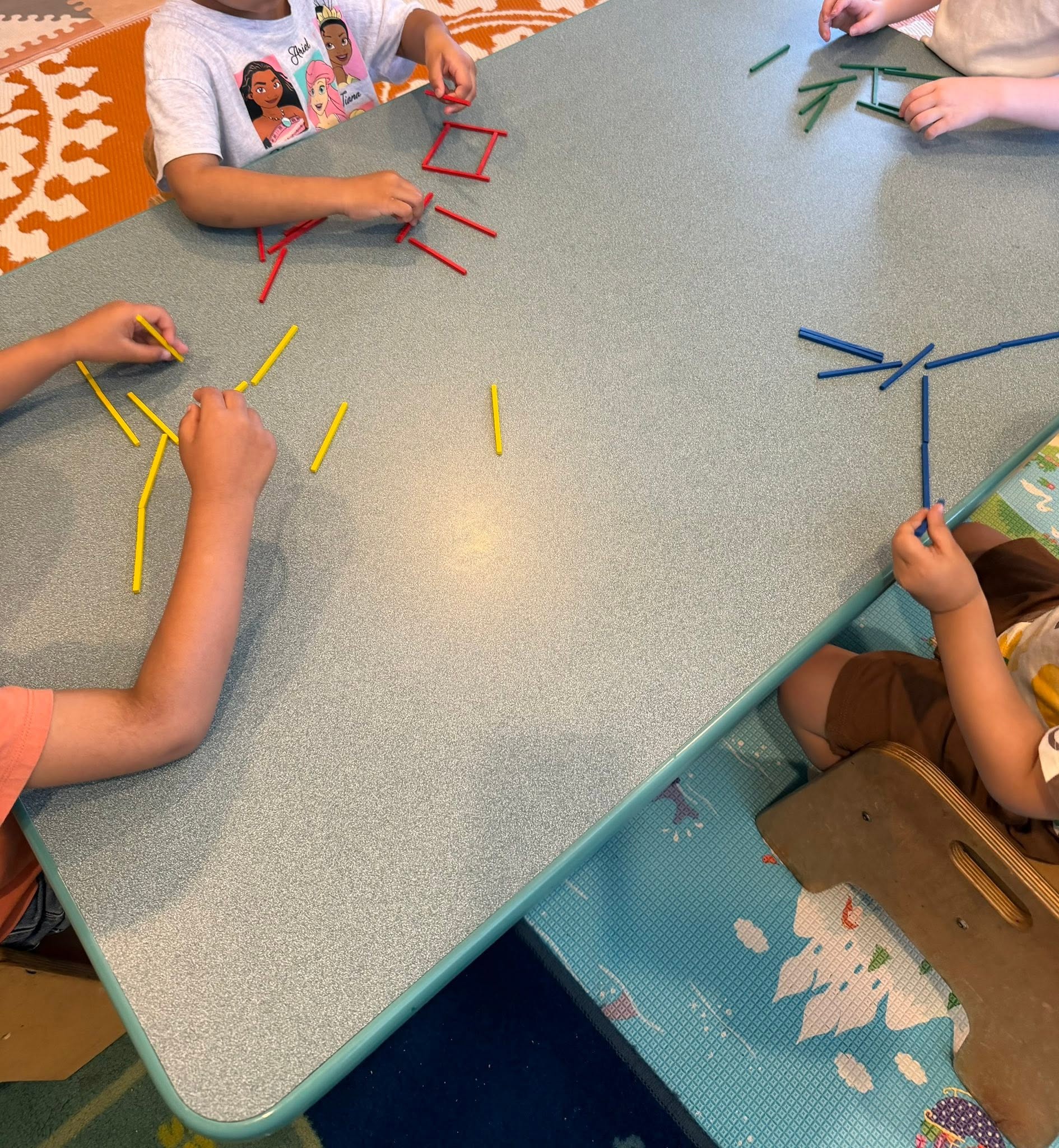 Children building shapes from colored counting sticks at a table