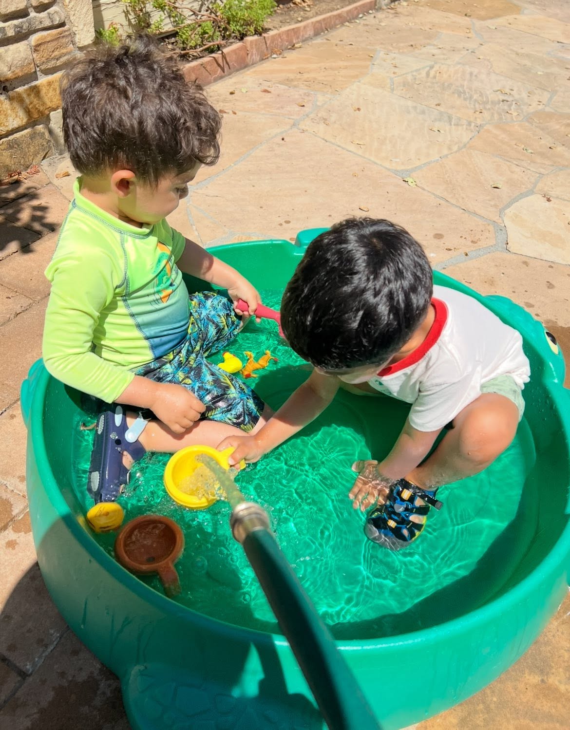 Two toddlers playing at an outdoor water table in the sunshine